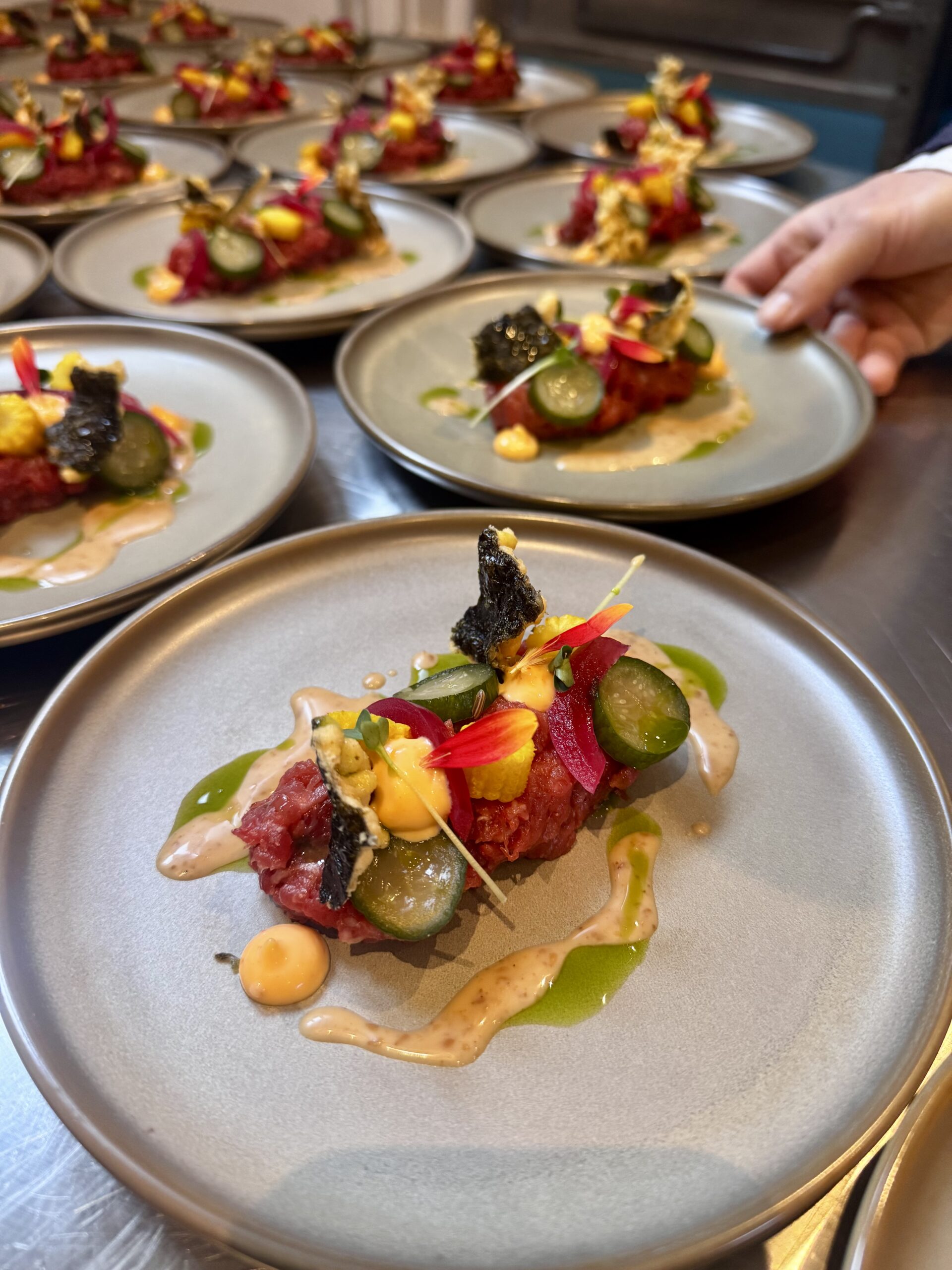 Rundertartaar met komkommer, crème en krokante garnituur op meerdere borden