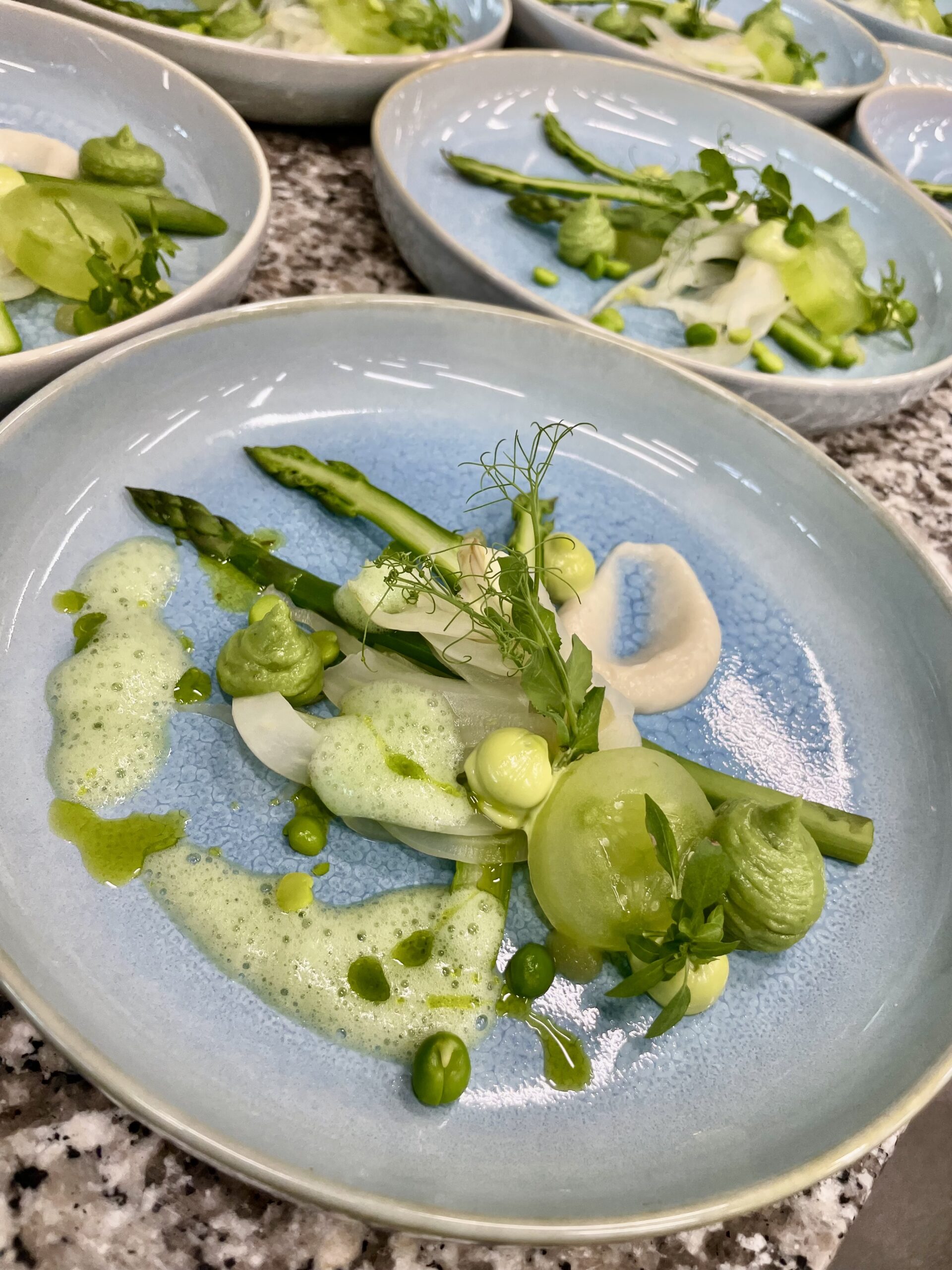 Fijn opgemaakt groentegerecht met asperge, venkel, erwtencrème en kruidenschuim op blauw bord